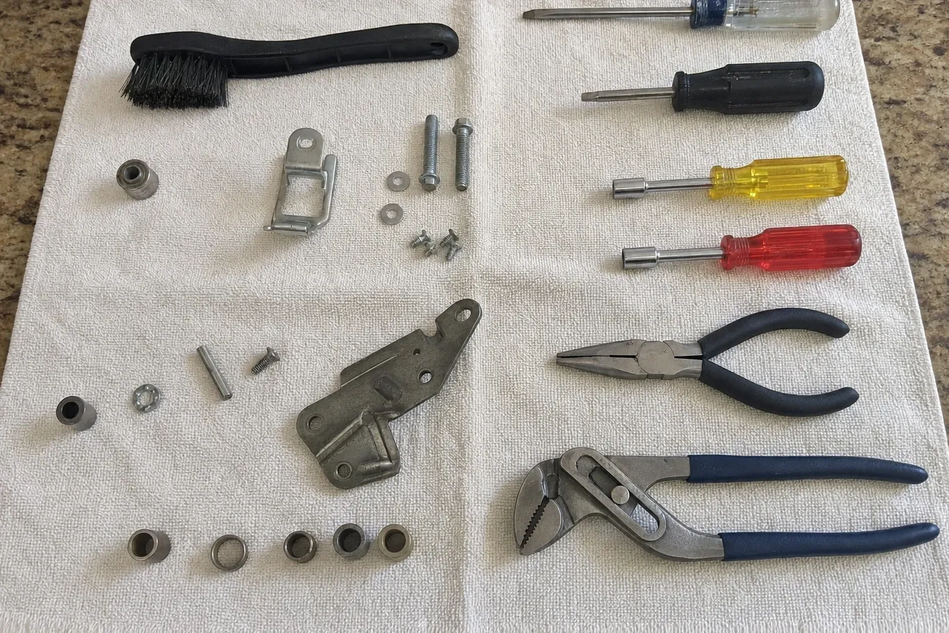 Hand tools laid out beside blower and hinge hardware — bushings, a bracket, screws and washers — on a towel over stone